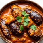 A bowl of rich, silken eggplant curry garnished with fresh herbs and spices.